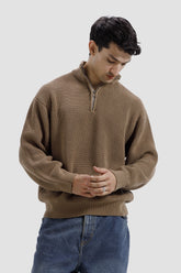 Man wearing a brown ribbed sweater and blue jeans on a light gray background