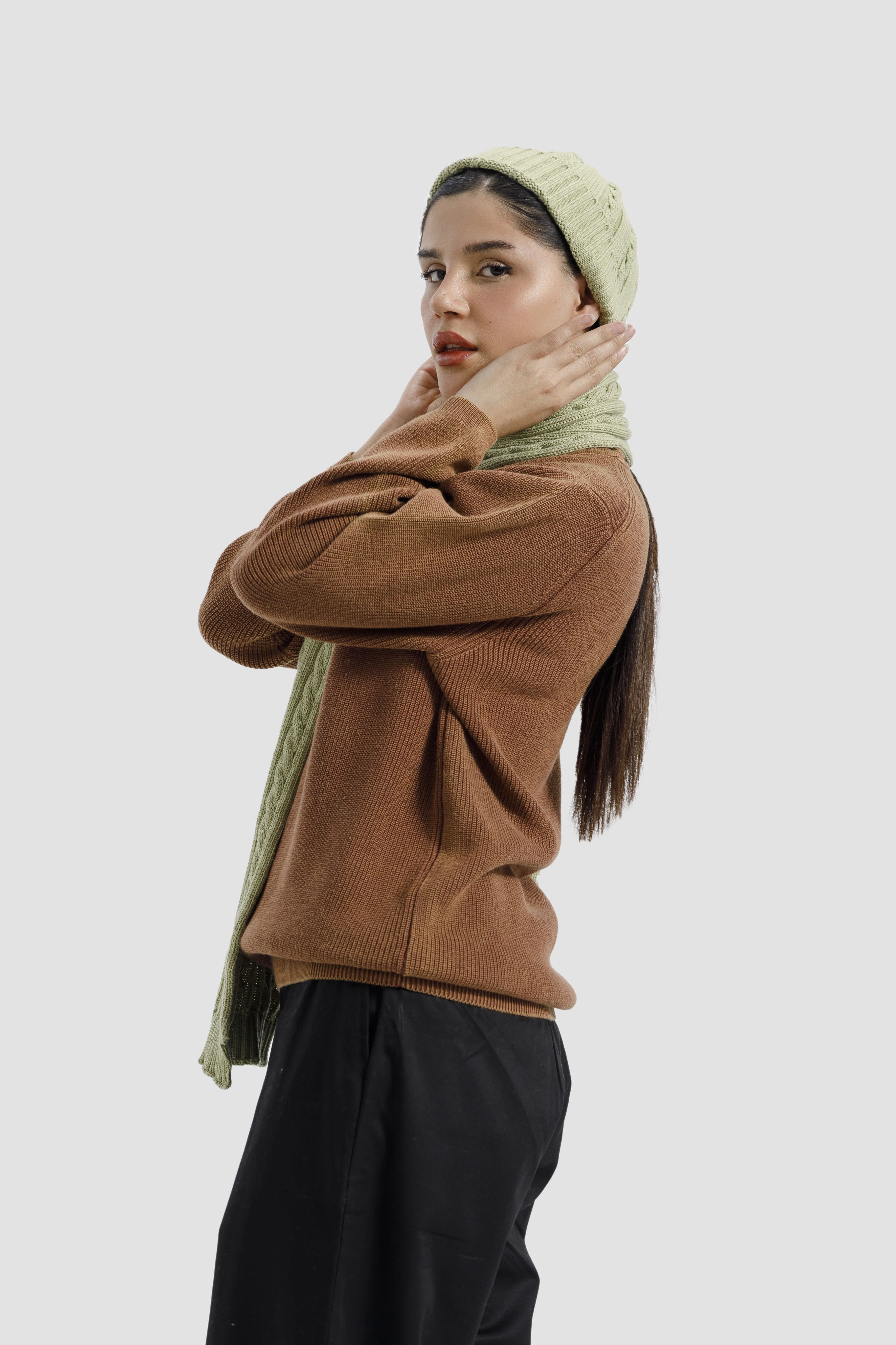Woman wearing a brown sweater and black pants with a green headscarf on a white background