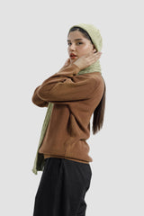 Woman wearing a brown sweater and black pants with a green headscarf on a white background