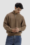 Man wearing a brown ribbed sweater and blue jeans on a light gray background