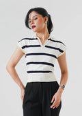 A woman modeling a short-sleeve polo shirt with horizontal black and off-white stripes, paired with black trousers and black heels, against a light gray studio background.